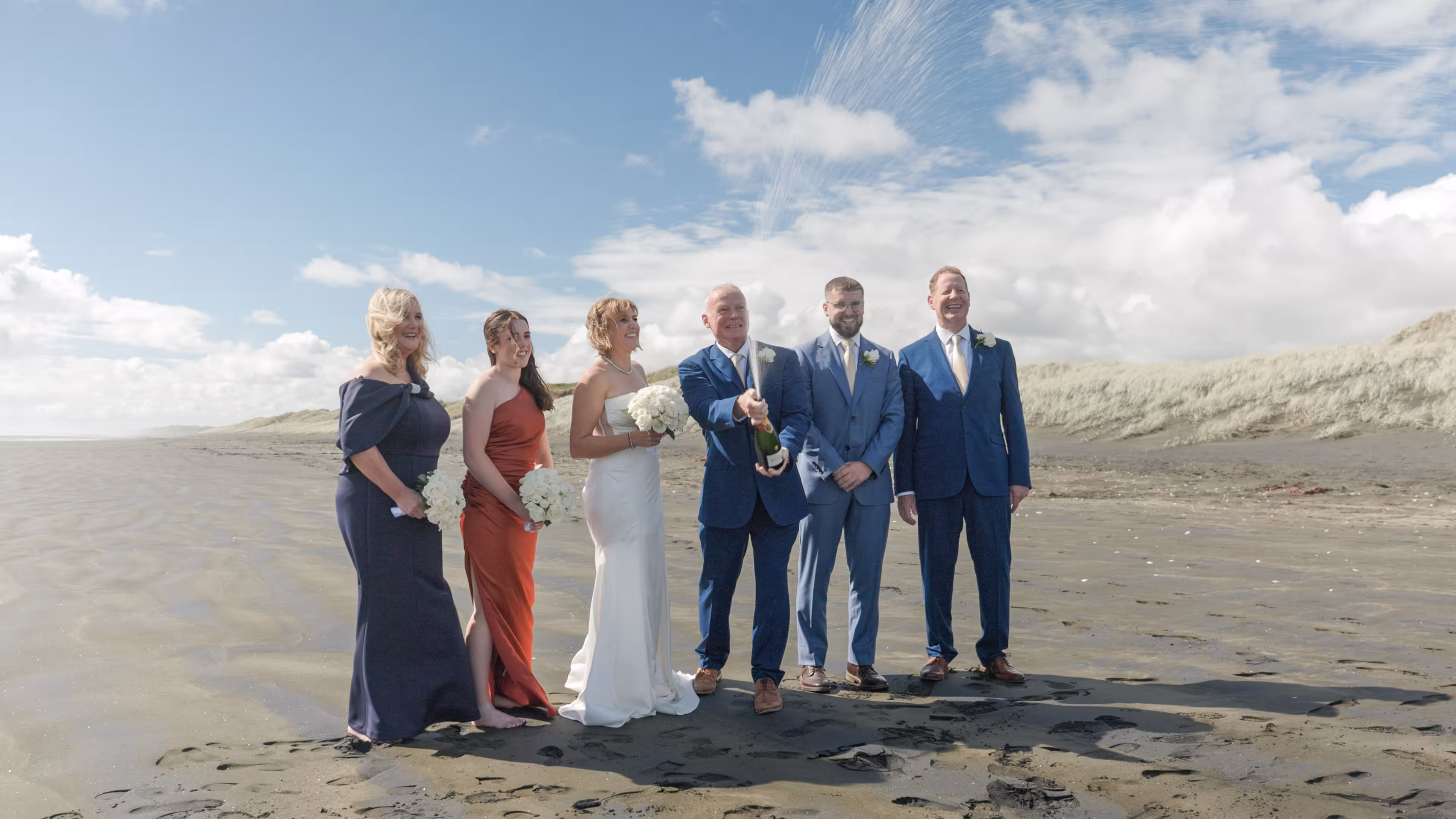 Wedding couple celebrating with champagne on Muriwai beach after ceremony