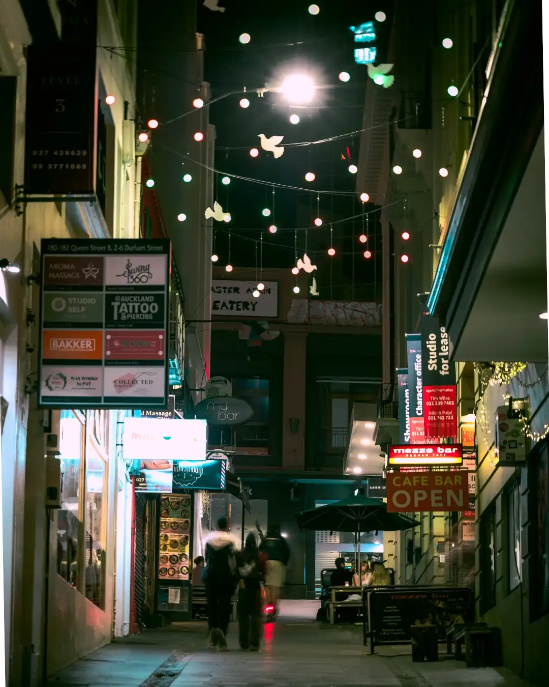 Narrow night alley with hanging lights and blurred pedestrians.