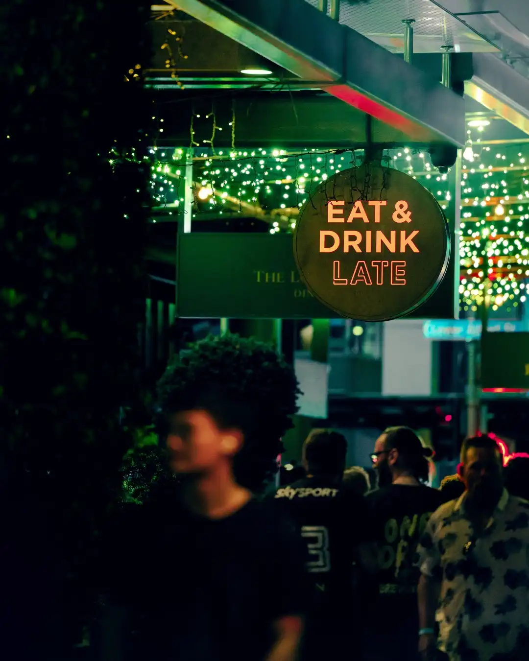 Neon Eat & Drink Late sign above a busy night street.