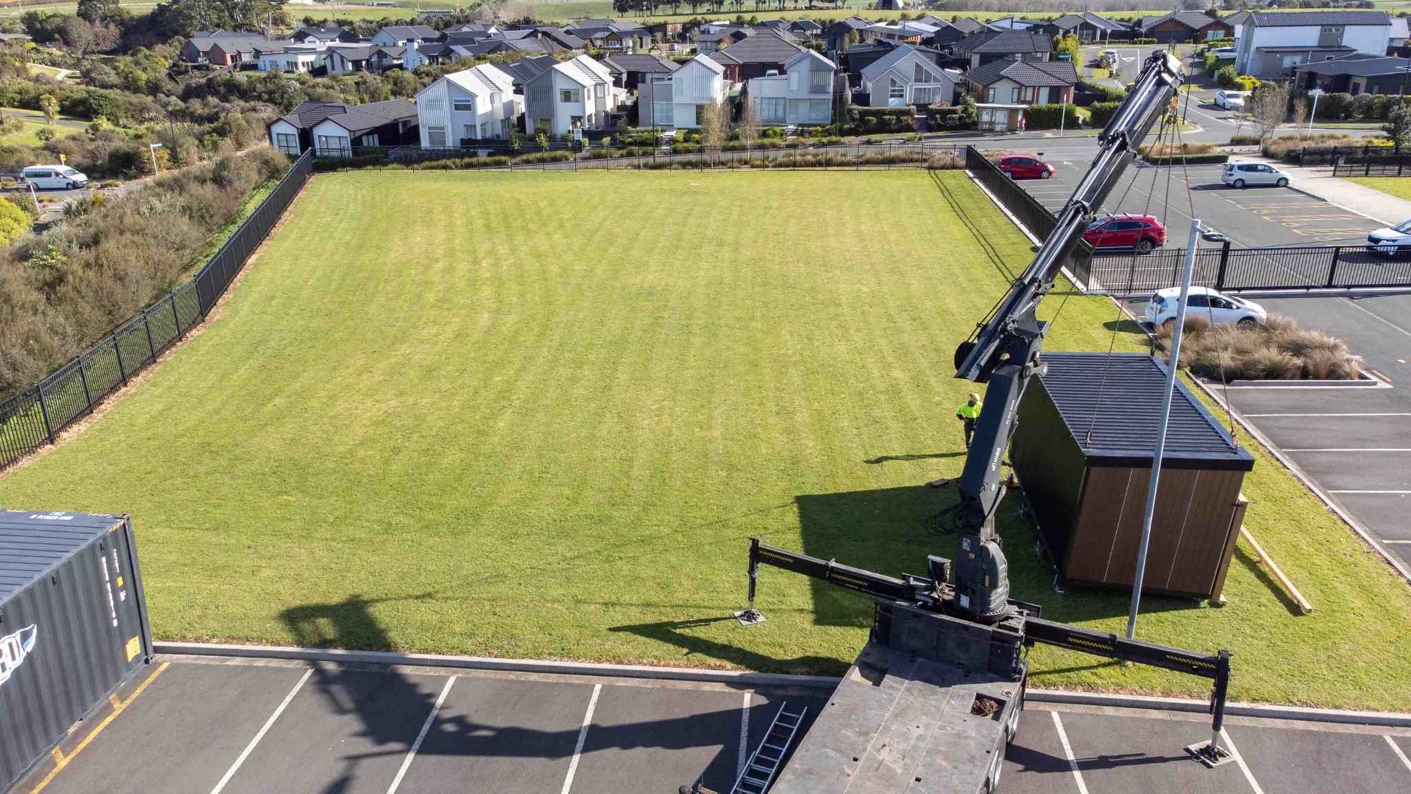 Drone image of Outclass Ltd modular building being lowered into position on a large grassy lot.