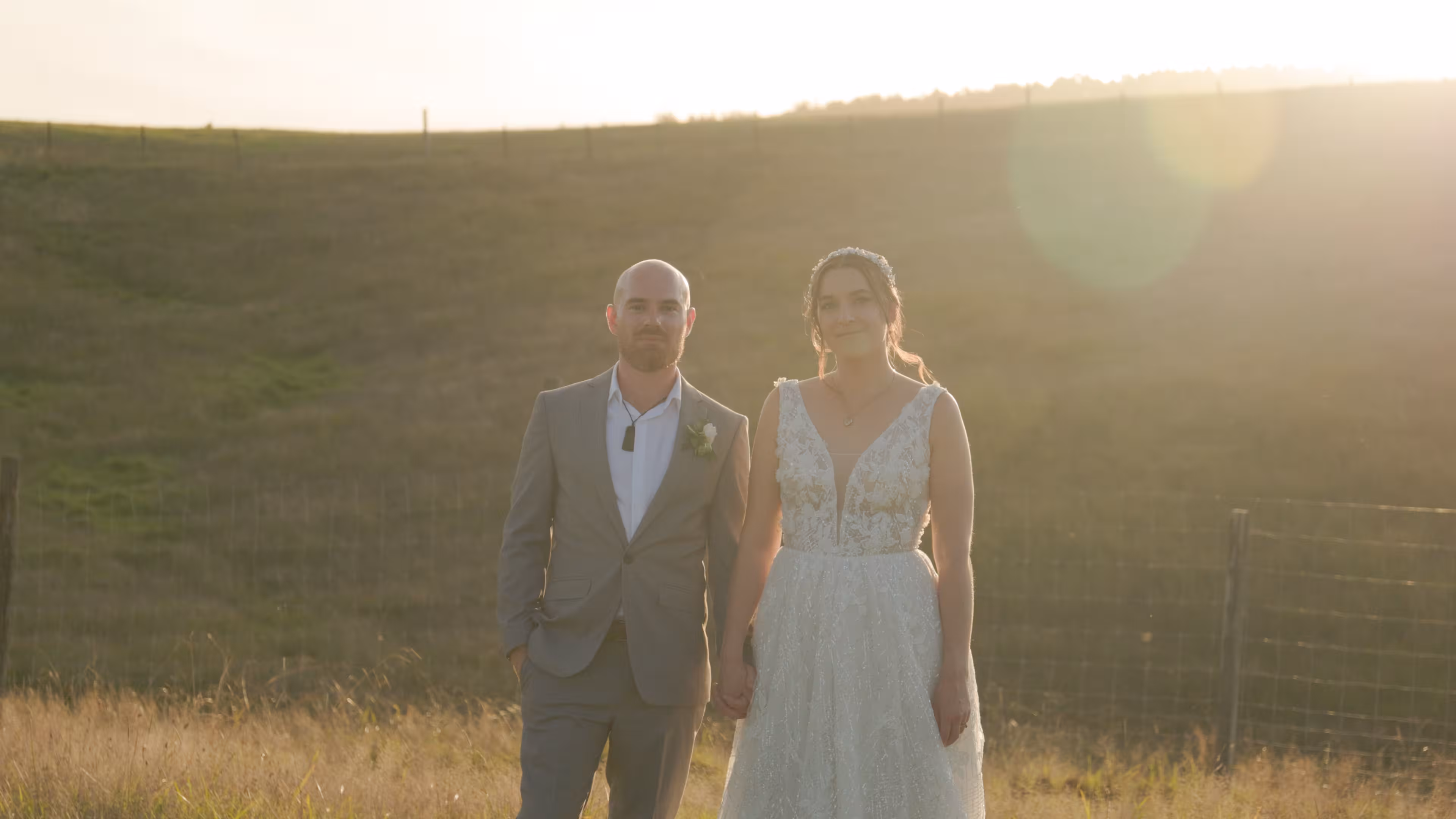 Bride and groom holding hands during golden hour portraits in a rolling New Zealand pastoral landscape at Waterfall Farm.