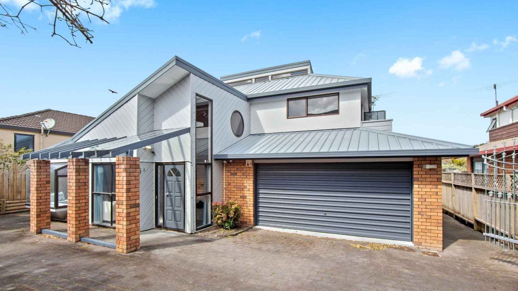 Street view of modern brick-and-cladding house with double garage and pitched roof.