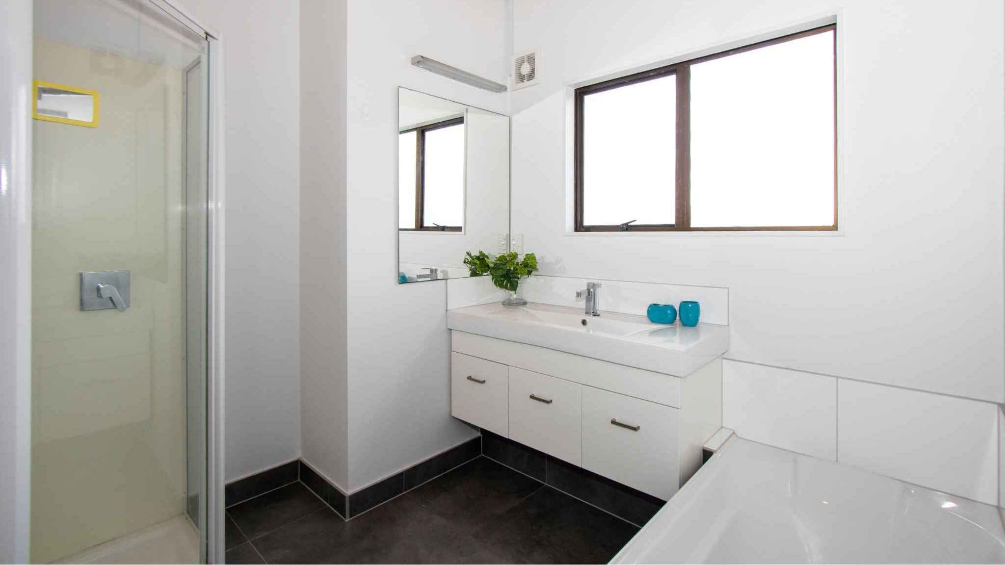Bright bathroom with walk-in shower, white vanity, large mirror, and natural light from window.